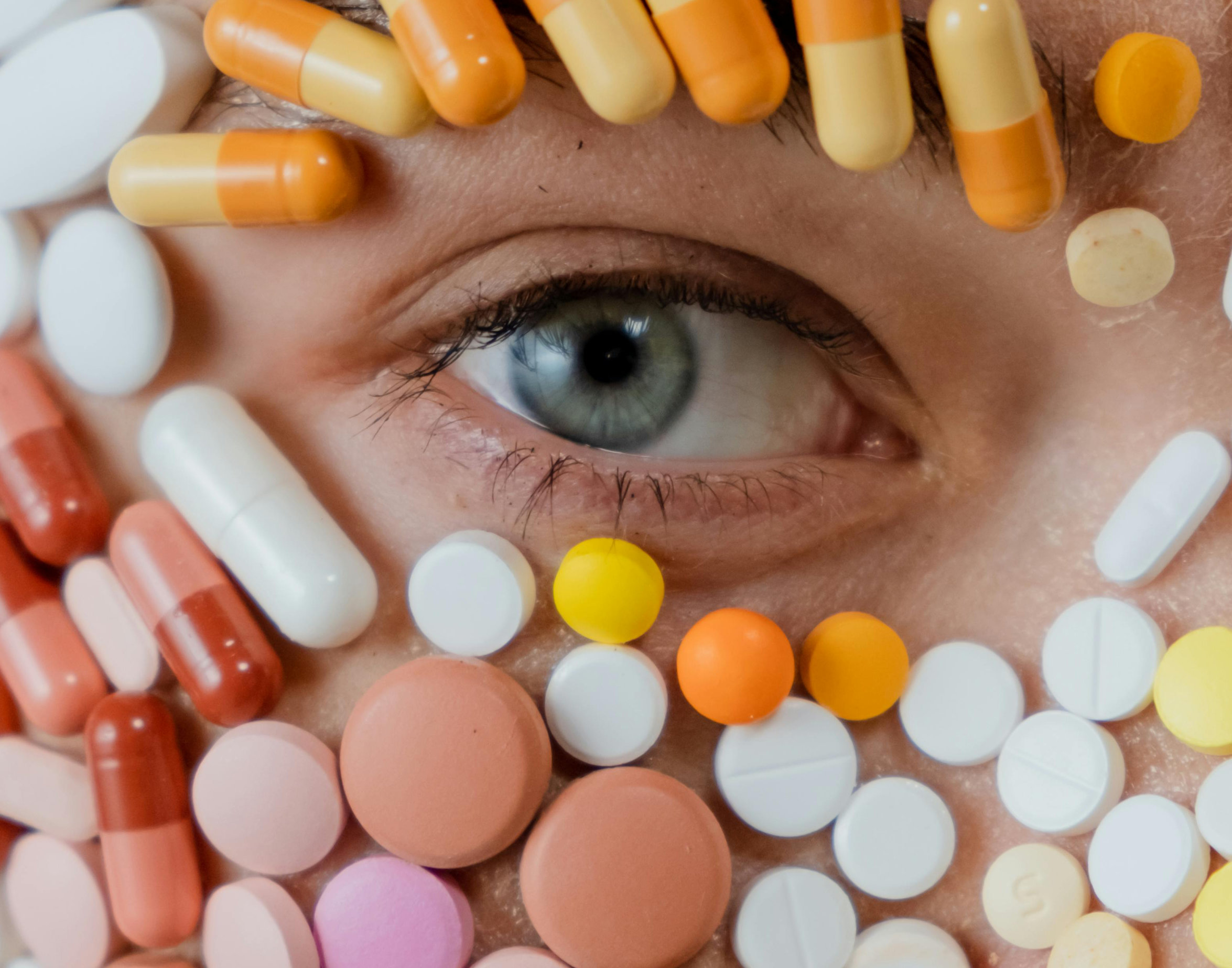 foto conceitual com parte de rosto humano coberto com comprimidos, ficando um olho aberto aparente